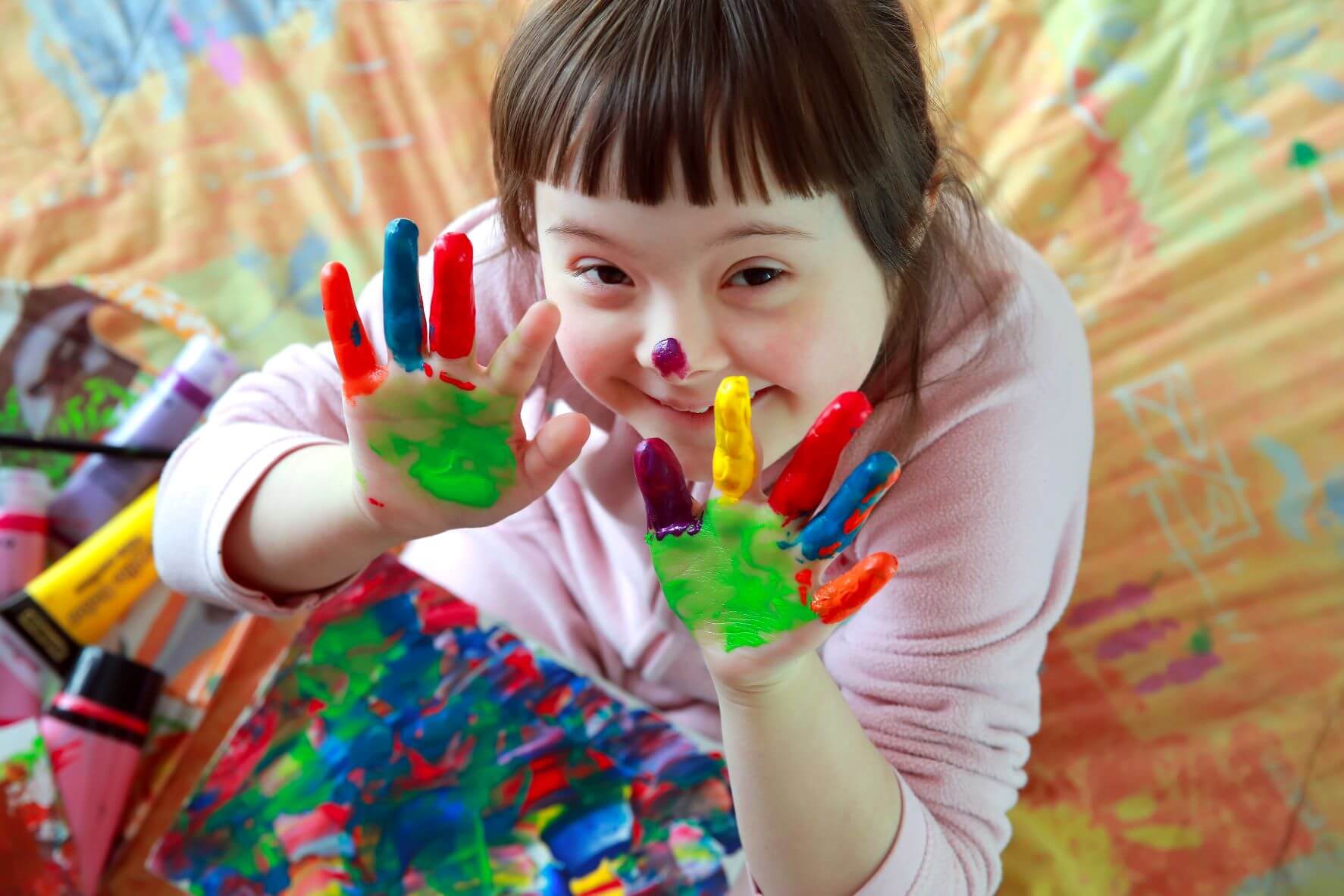 Smiling girl with painted hands on a colourful background