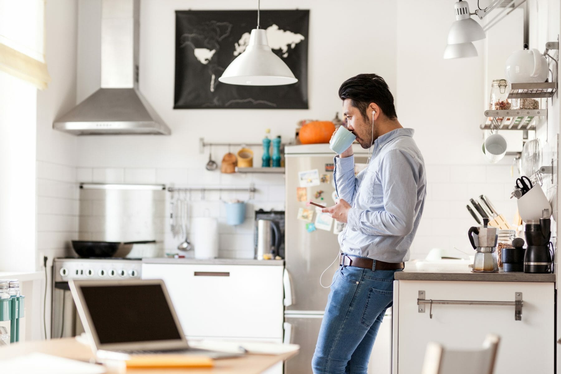 Man in kitchen sipping a coffee with headphones in looking at his phone