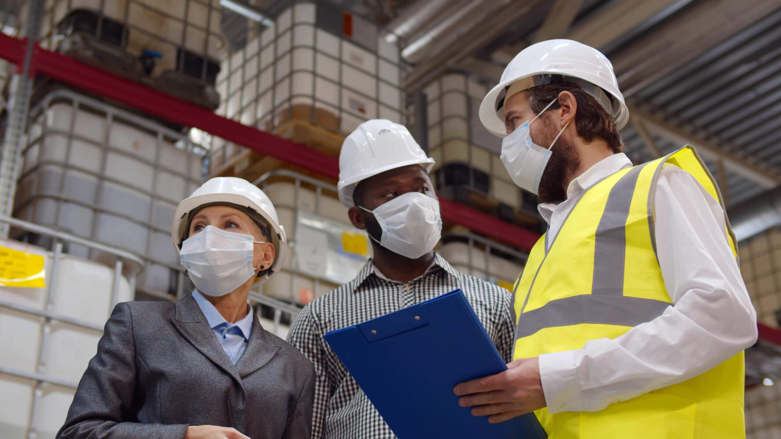 Diverse warehouse inspectors wearing safety mask discussing distribution plan on clipboard
